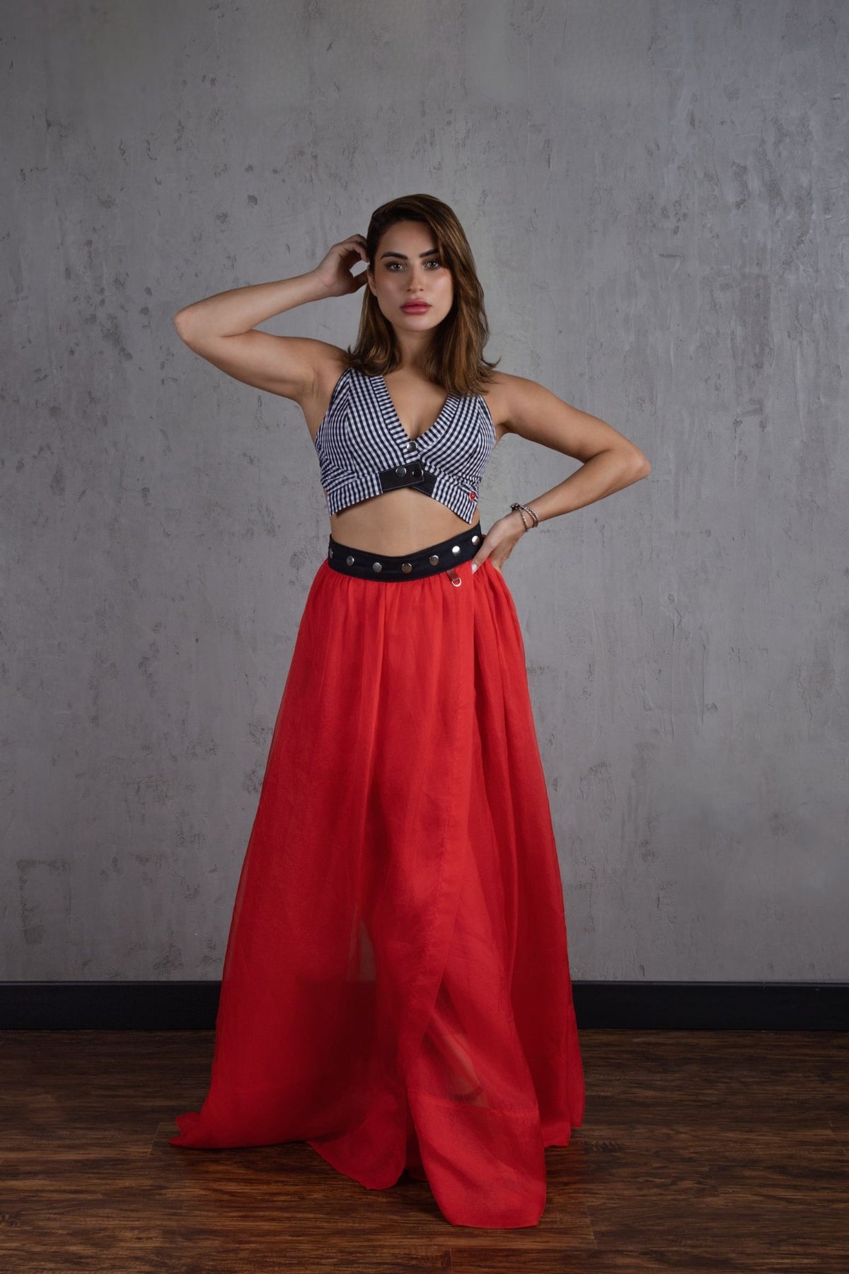 Woman wearing a patterned top and red skirt against a gray wall.