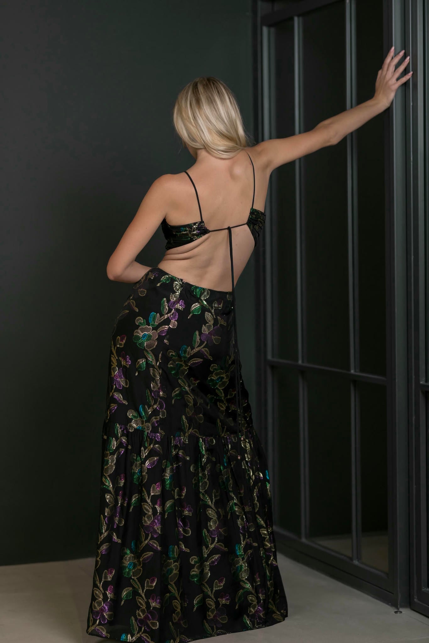 Woman in a black floral dress standing against a dark wall.