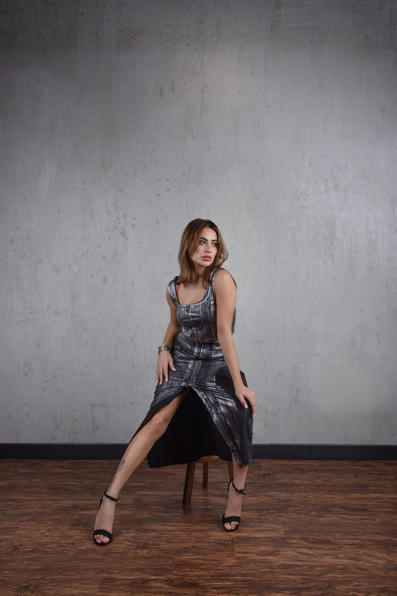 Woman in a metallic dress posing against a gray wall.