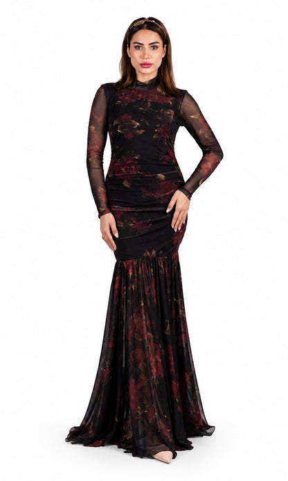 A woman modeling a floor-length black evening gown with sheer long sleeves and a dark red floral print, set against a plain white background.
