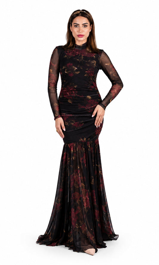 A woman modeling a floor-length black evening gown with sheer long sleeves and a dark red floral print, set against a plain white background.