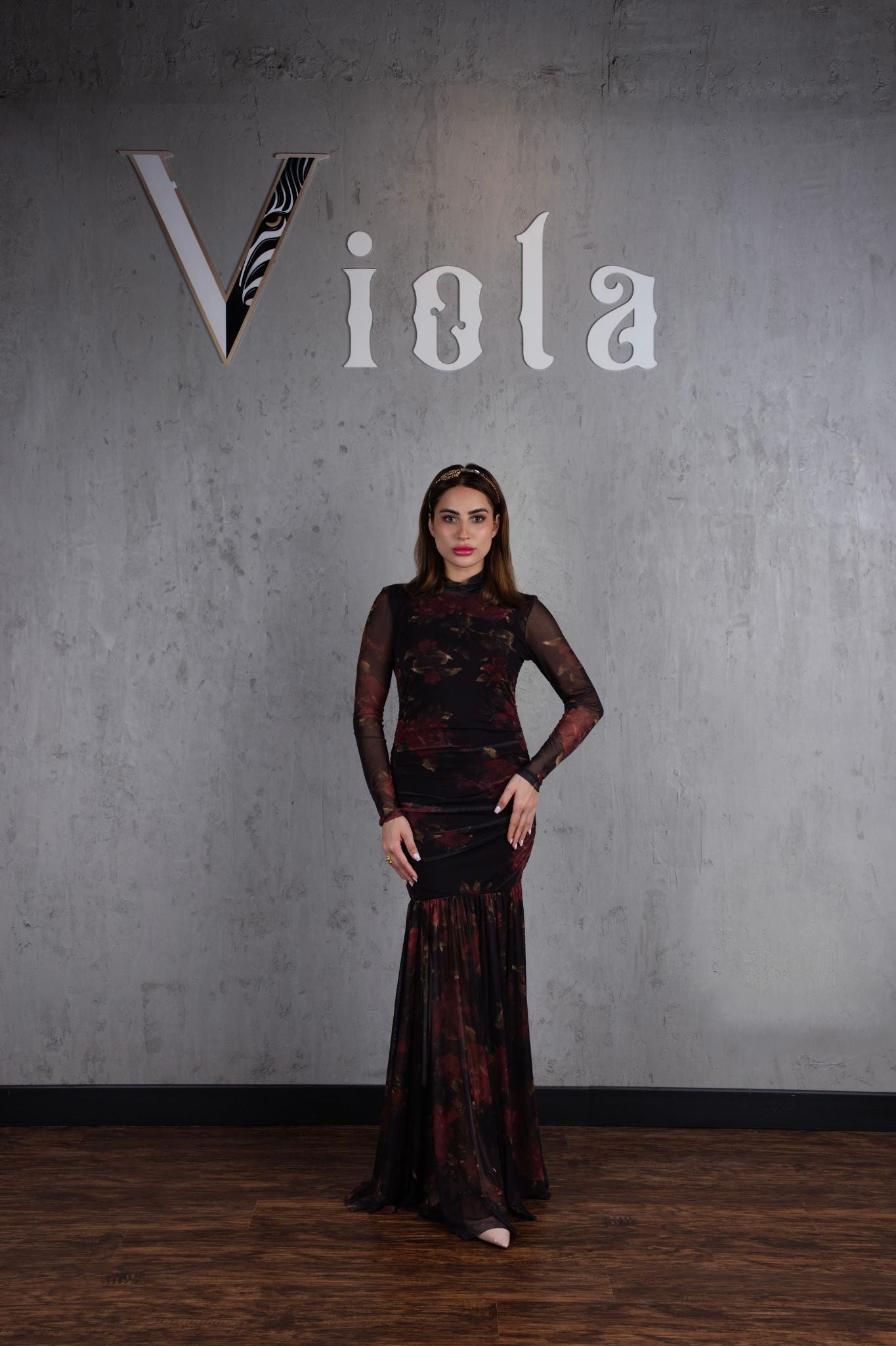 Woman in a dark patterned dress standing against a gray wall with 'Viola' branding.