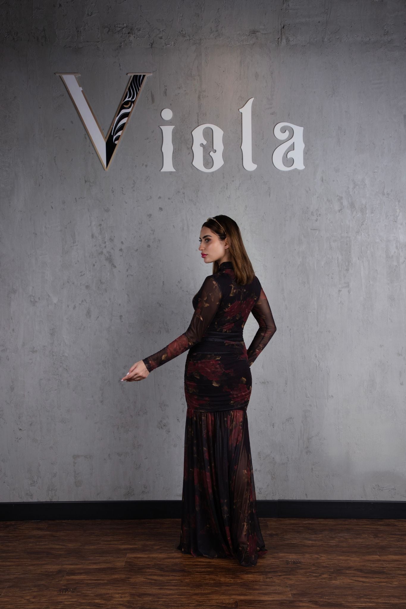 Woman in a dark patterned dress standing against a gray wall with 'Viola' branding.