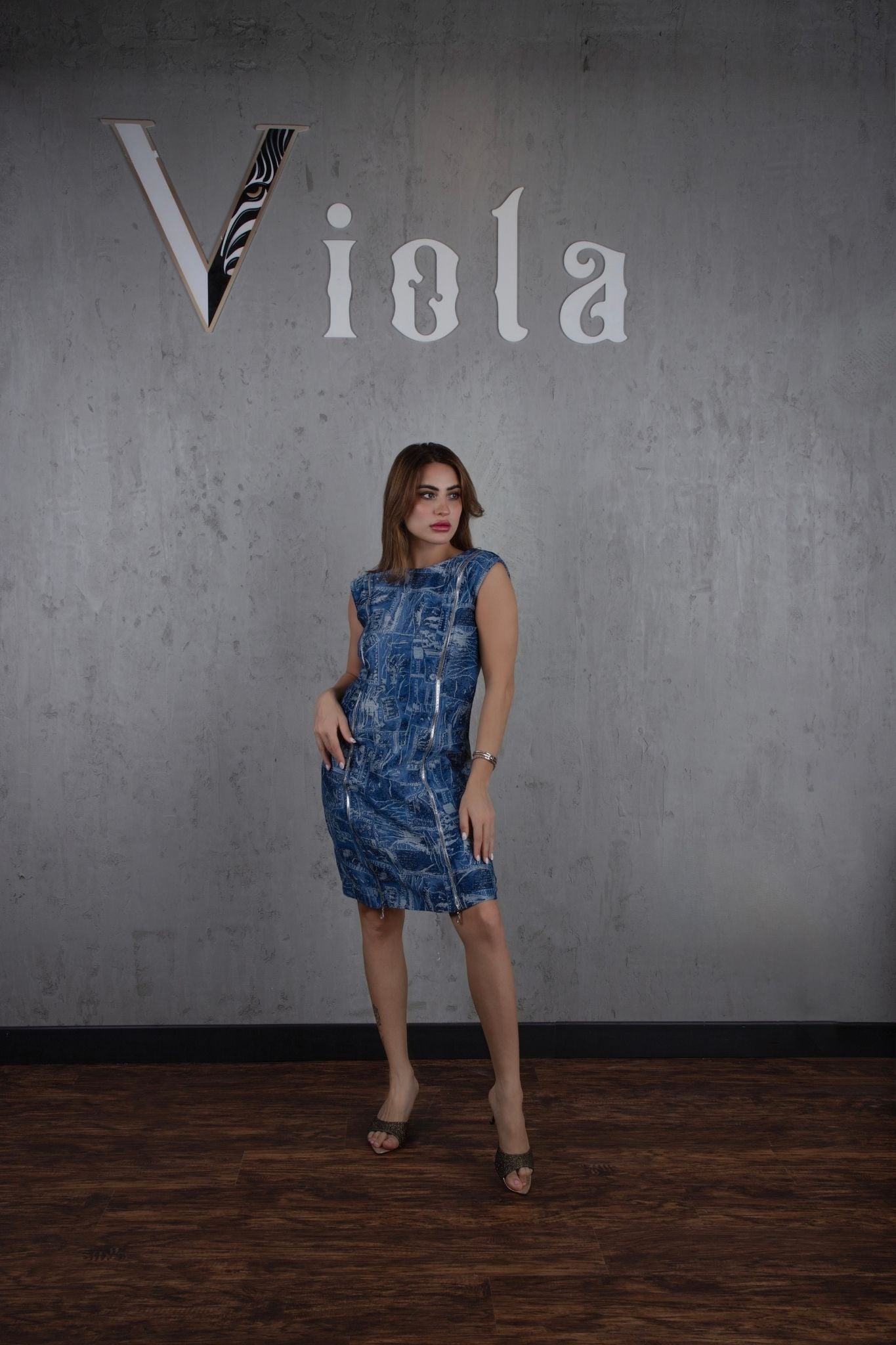 Woman in a blue dress standing against a gray wall with 'Viola' branding.