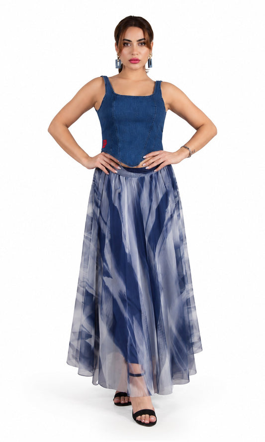 A woman modeling a sleeveless maxi dress with a dark blue velvet-like bodice and a flowing sheer skirt with a blue and gray abstract watercolor pattern, set against a plain white studio background.