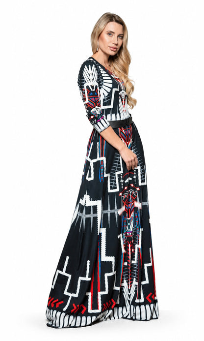 A woman modeling a long black maxi dress with a bold geometric and tribal-inspired pattern in white, red, and blue, set against a plain white studio background.
