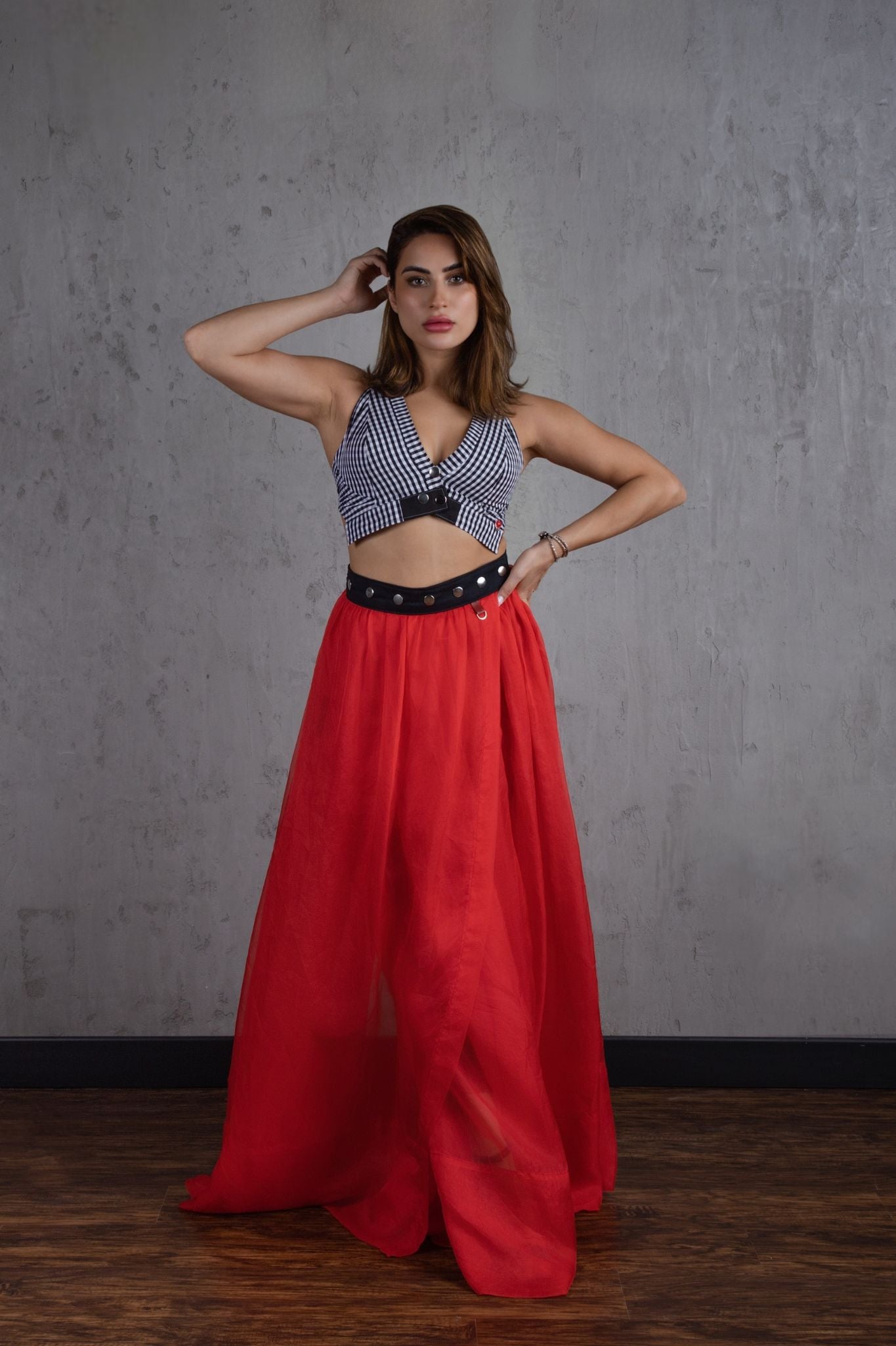 Woman wearing a patterned top and red skirt against a gray wall.