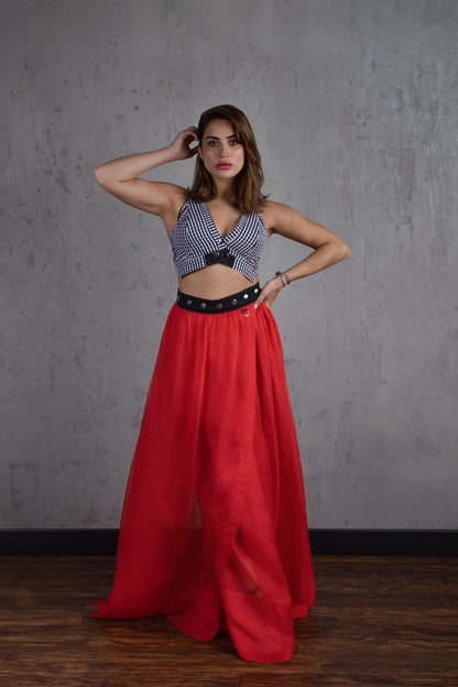 Woman wearing a patterned top and red skirt against a gray wall.