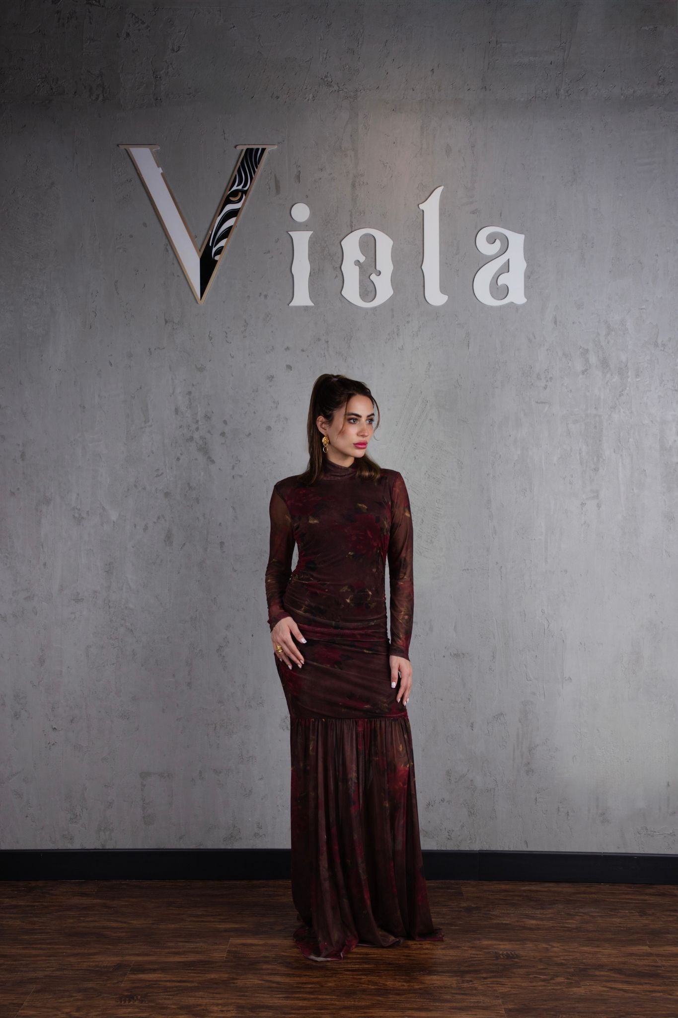 Woman in a dark red dress standing against a gray wall with 'Viola' branding.