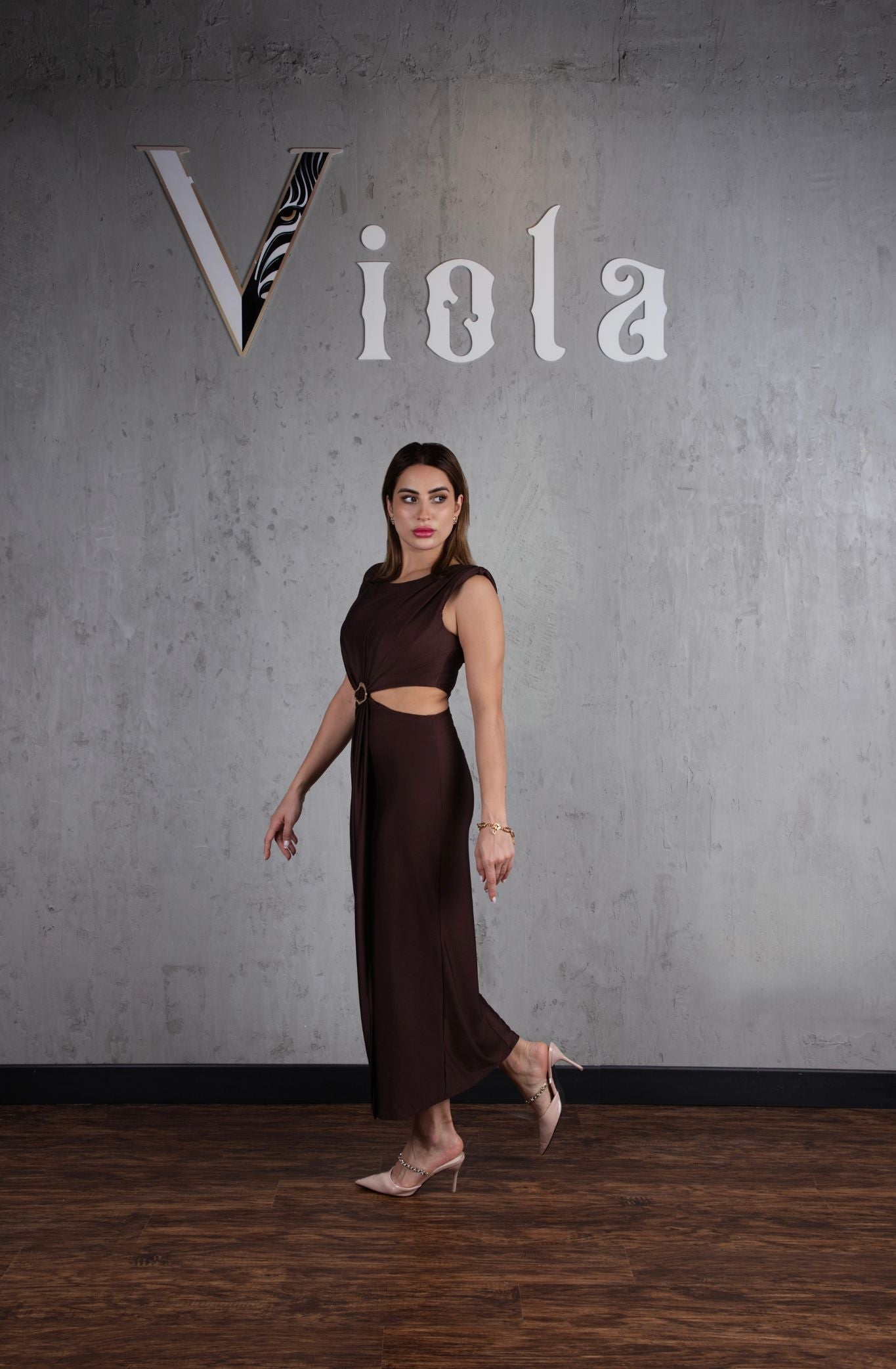 Woman in a brown dress standing against a gray wall with 'Viola' branding.