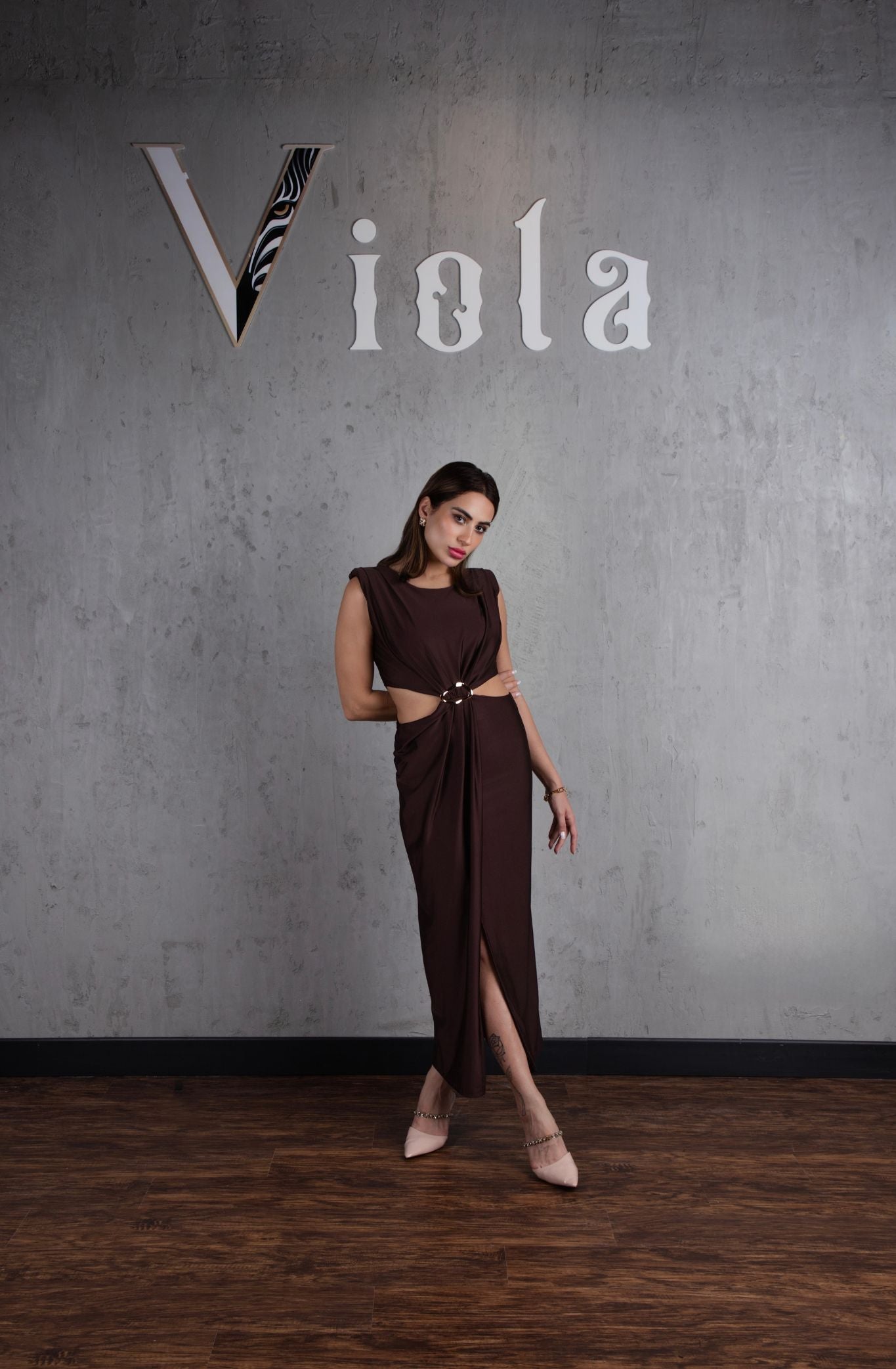 Woman in a brown dress standing against a gray wall with 'Viola' branding.