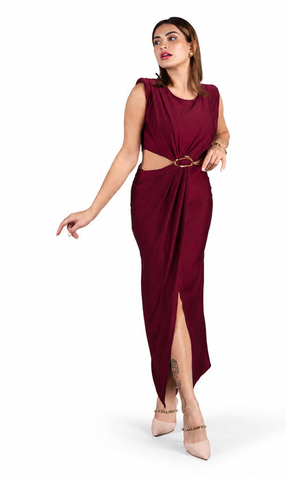 A woman models a sleeveless, deep burgundy maxi dress with a cutout at the waist, a gold ring accent, and a high side slit. She is wearing nude heels and standing against a plain white background.