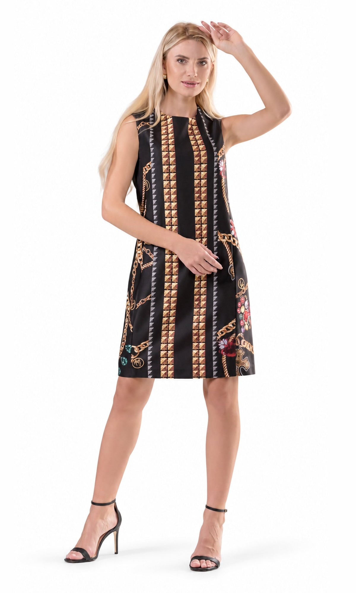 A woman modeling a sleeveless black A-line dress with vertical gold chain and coin-like patterns, shown against a plain white studio background.