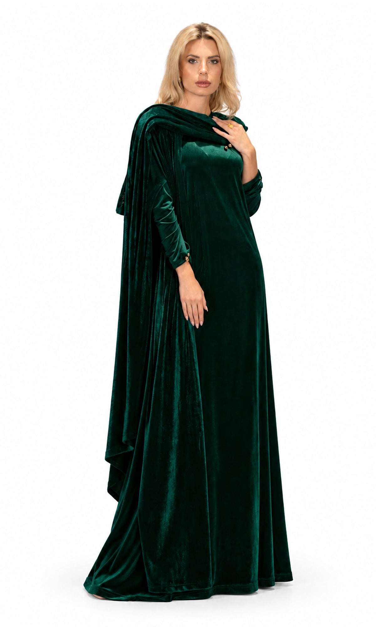 A woman modeling a floor-length emerald green velvet gown with draped cape-style sleeves and a high-low hemline, photographed against a plain white studio background.