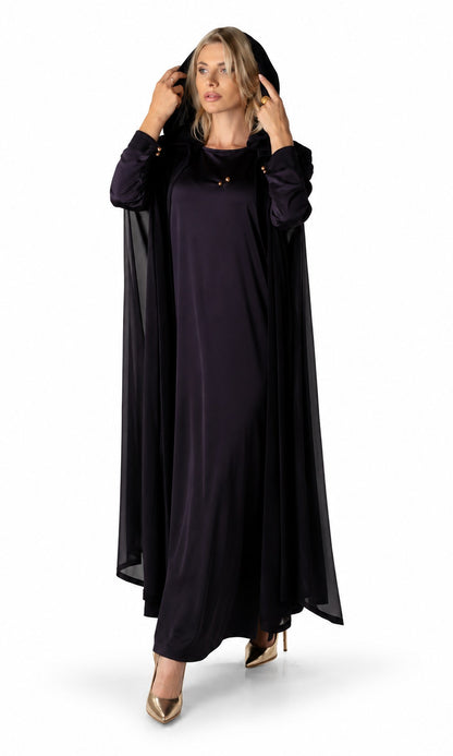 A woman modeling a long, flowing black dress with matching sheer draped sleeves and a matching head covering, styled with gold high heels against a plain white studio background.