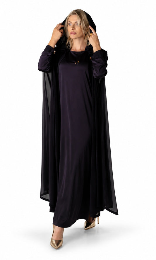 A woman modeling a long, flowing black dress with matching sheer draped sleeves and a matching head covering, styled with gold high heels against a plain white studio background.