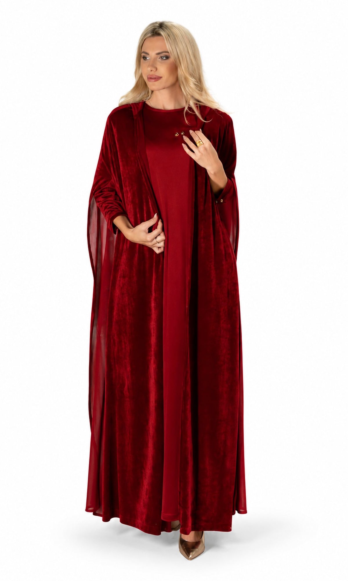 A woman modeling a long, floor-length burgundy velvet gown with draped cape sleeves, standing against a plain white studio background.