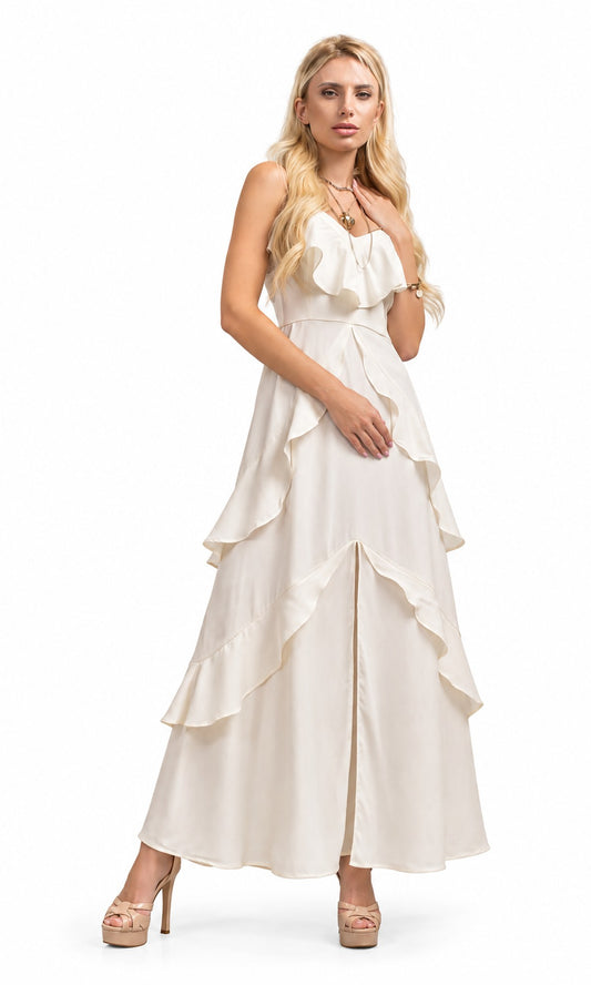 A blonde model wearing a long, sleeveless cream-colored dress with a ruffled sweetheart neckline, a defined waist, and layered ruffle tiers cascading down the skirt, paired with beige high-heeled sandals against a plain white background.