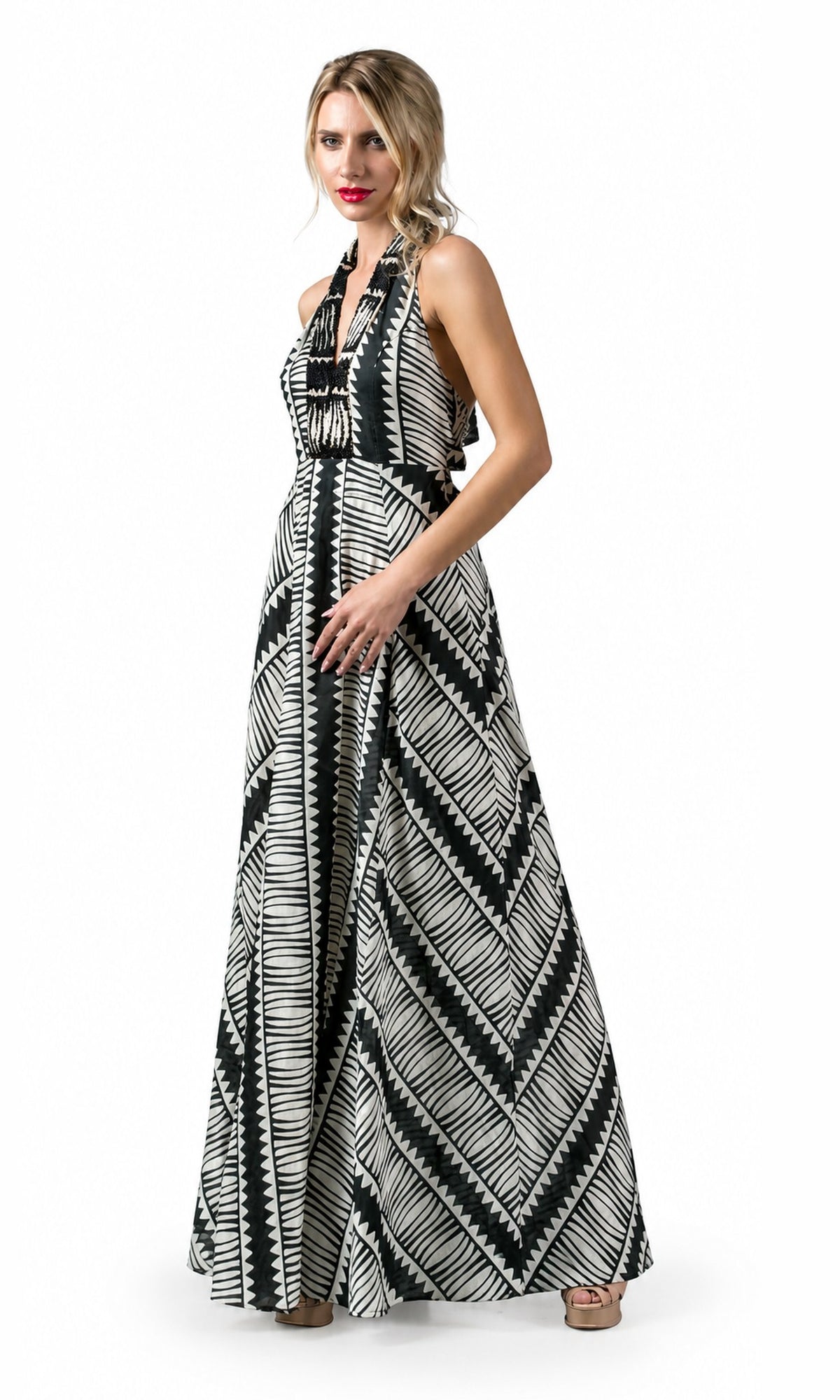 A woman modeling a sleeveless halter-neck maxi dress with a bold black and white geometric tribal pattern, set against a plain white studio background.