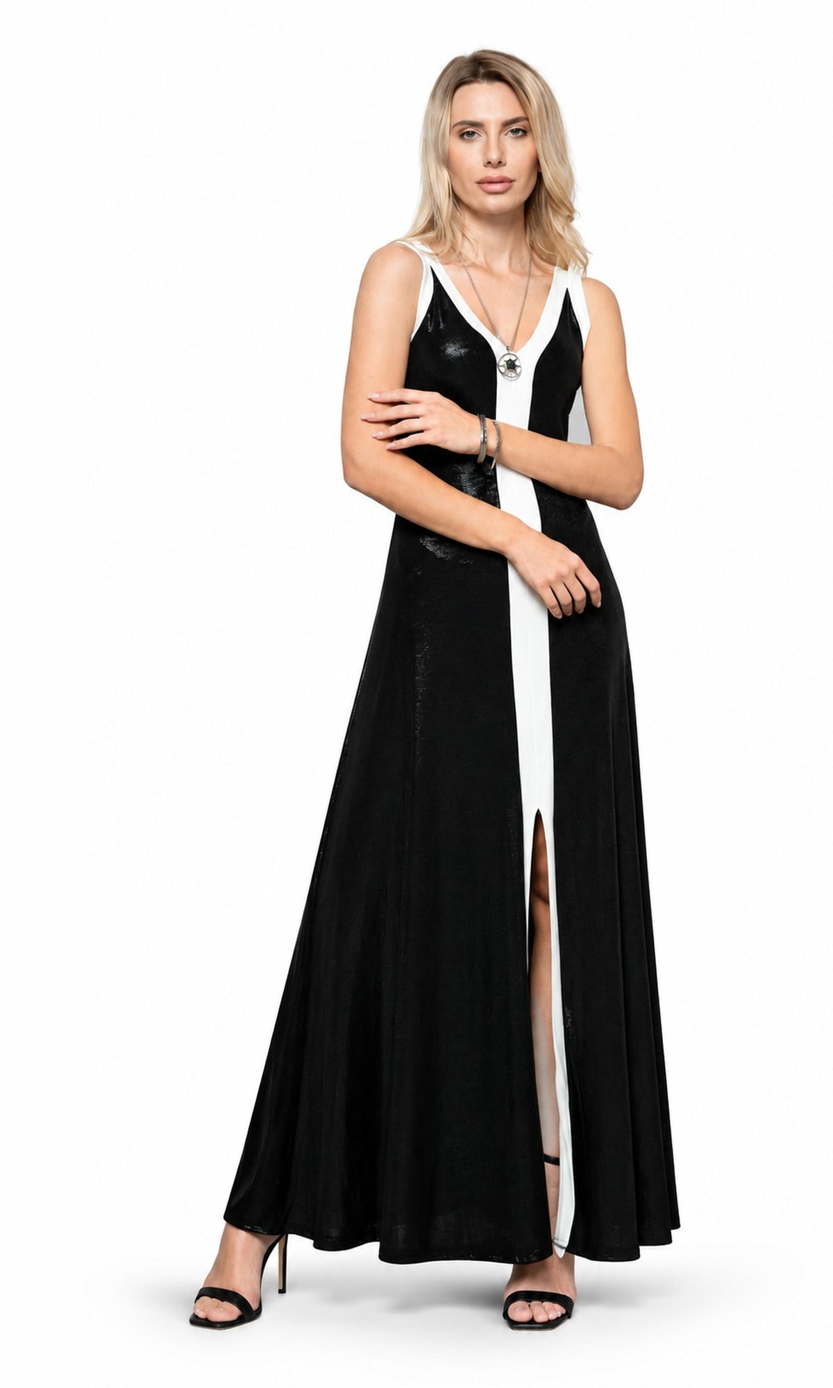 A woman modeling a sleeveless black and white maxi dress with a high front slit, photographed against a plain white studio background.