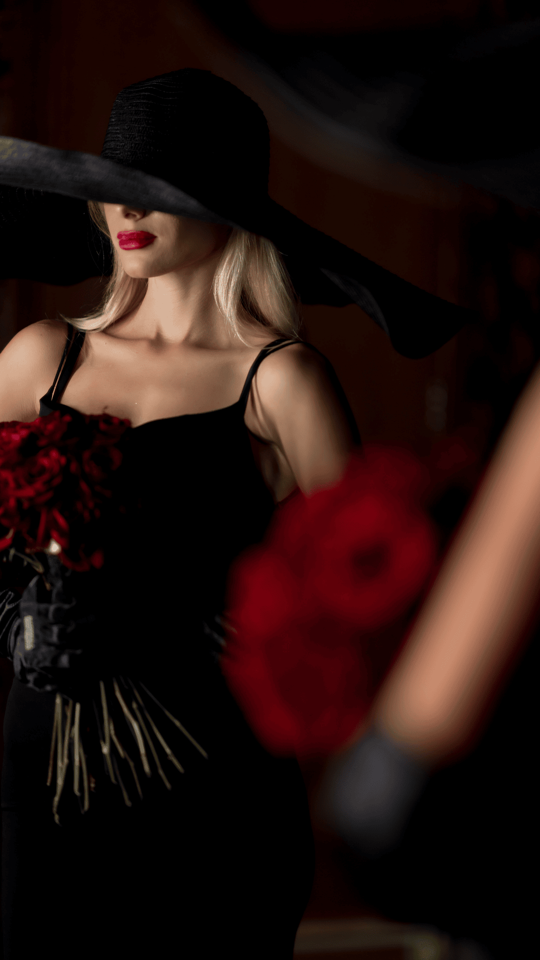 Woman in a black dress and hat with red roses, blurred background
