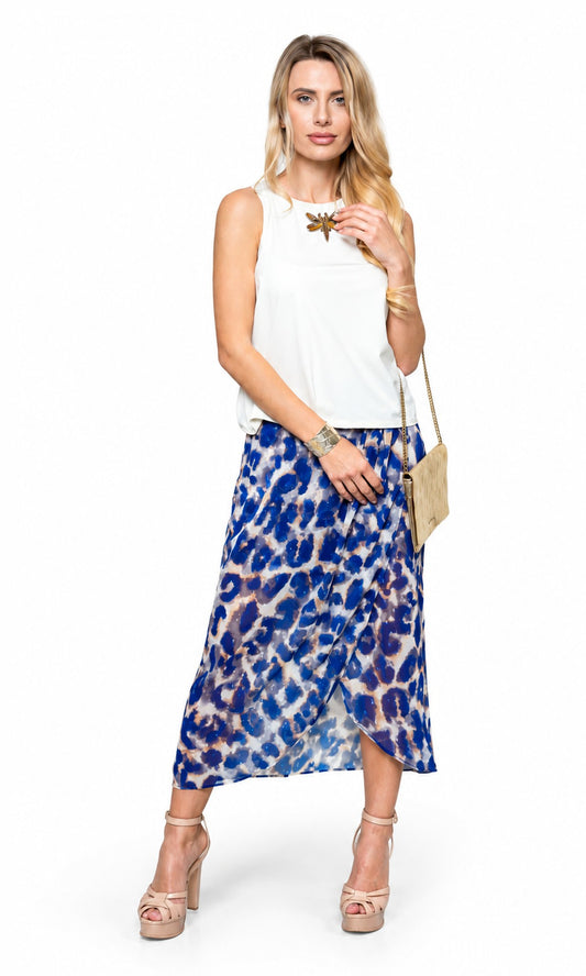 A woman modeling a sleeveless white top and a blue and white abstract patterned midi skirt, styled with a gold necklace, bracelet, and a small beige shoulder bag against a plain white background.