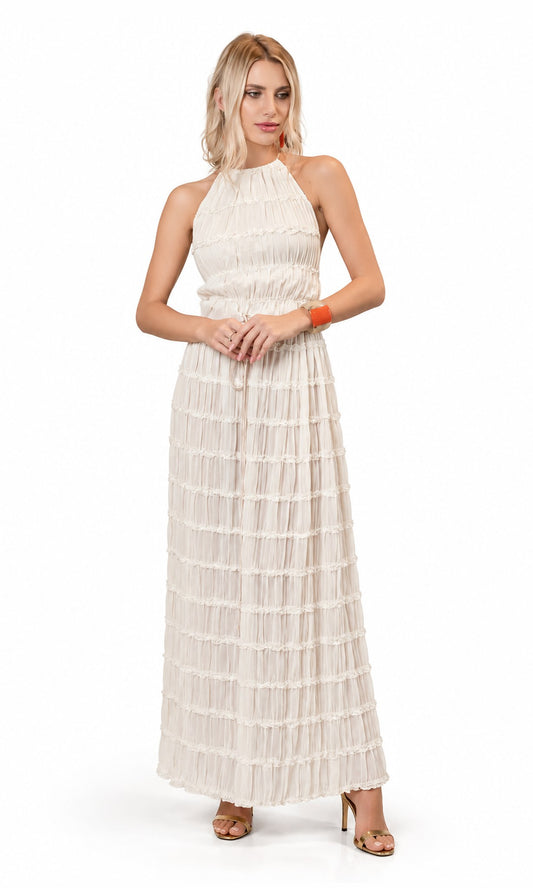 A woman modeling a sleeveless, halter-neck maxi dress in a warm off-white or cream color, featuring a tiered ruffled skirt. She is standing against a seamless white studio background.